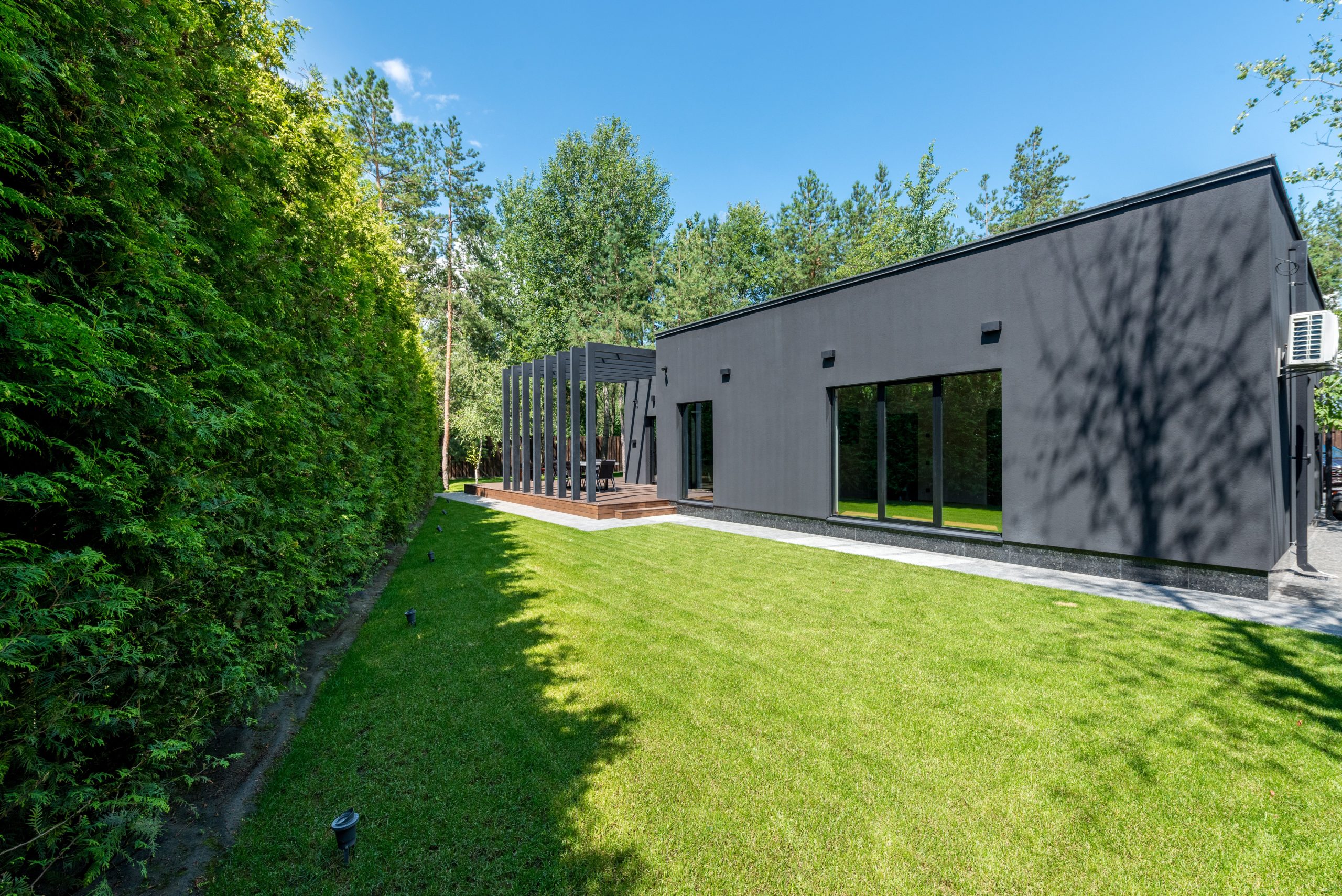 Sleek modern black home with large windows, green lawn, and surrounding trees